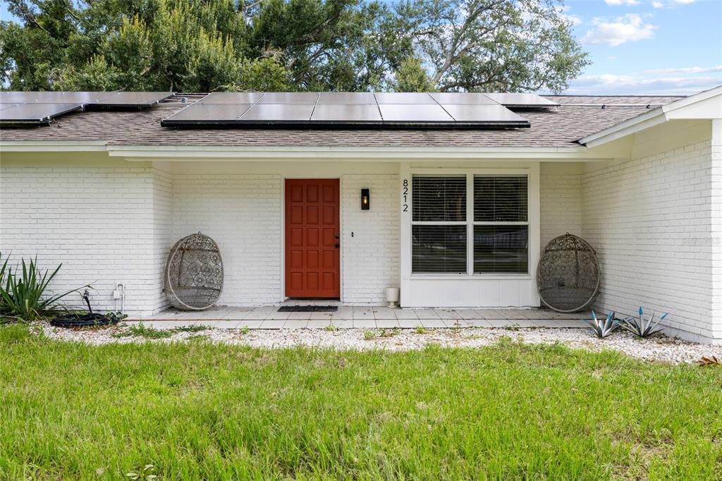 A white brick house exterior features a red front door, solar panels, and two hanging chairs — 8212 SUNNY VALE PLACE, TAMPA, FL
