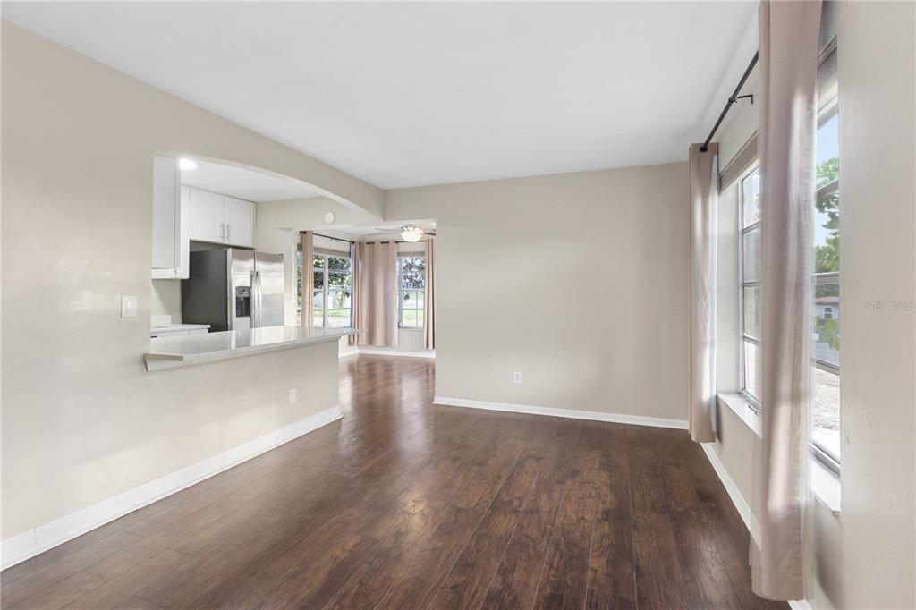 A living room with dark wood-look flooring, beige walls, a large window, and a door — 7045 FIRESIDE STREET, SPRING HILL, FL