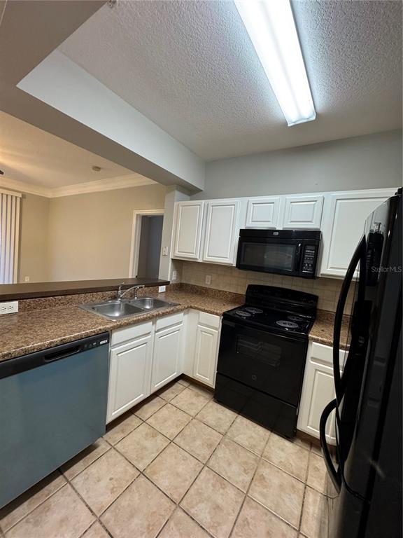 A kitchen features white cabinets, black appliances, granite countertops, and light-colored tile flooring — 12831 MADISON POINTE CIRCLE UNIT 104, ORLANDO, FL