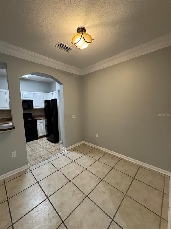 A dining area with beige tile floors and a light fixture leads into a kitchen — 12831 MADISON POINTE CIRCLE UNIT 104, ORLANDO, FL