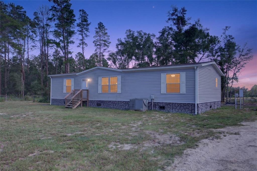 A light gray storage shed sits on a grassy lot surrounded by pine trees — 79 NE 91ST STREET, BRANFORD, FL