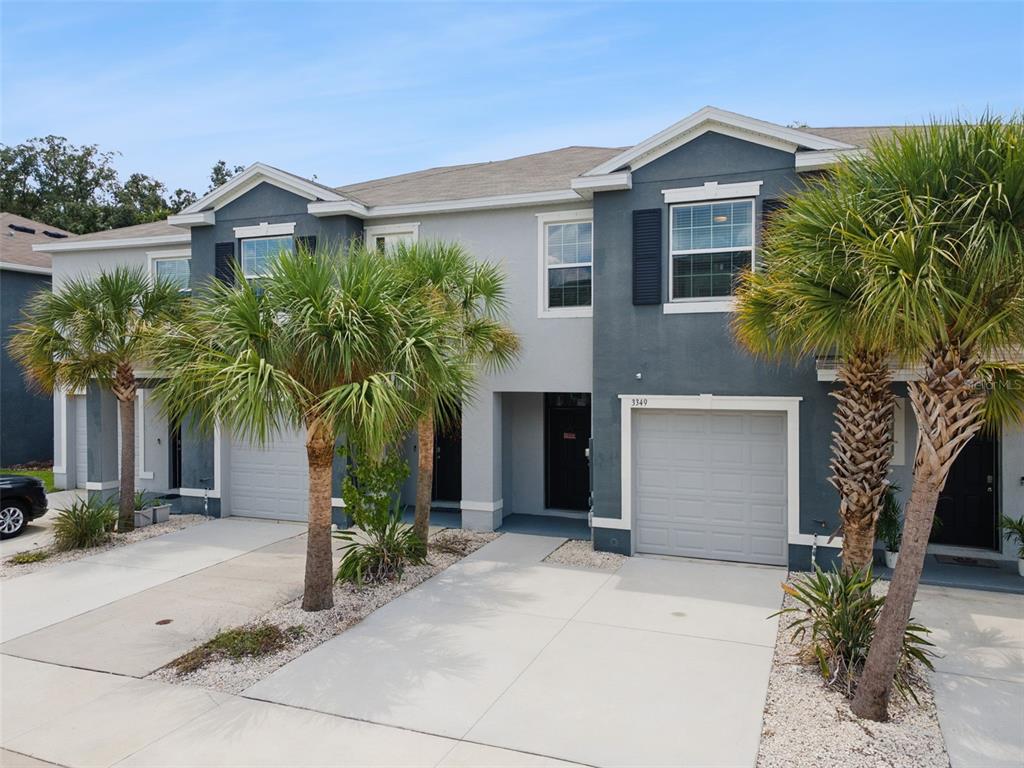 A two-story townhouse exterior features gray siding, a concrete driveway, and several palm trees — 3349 PLEASANT WILLOW COURT, BRANDON, FL