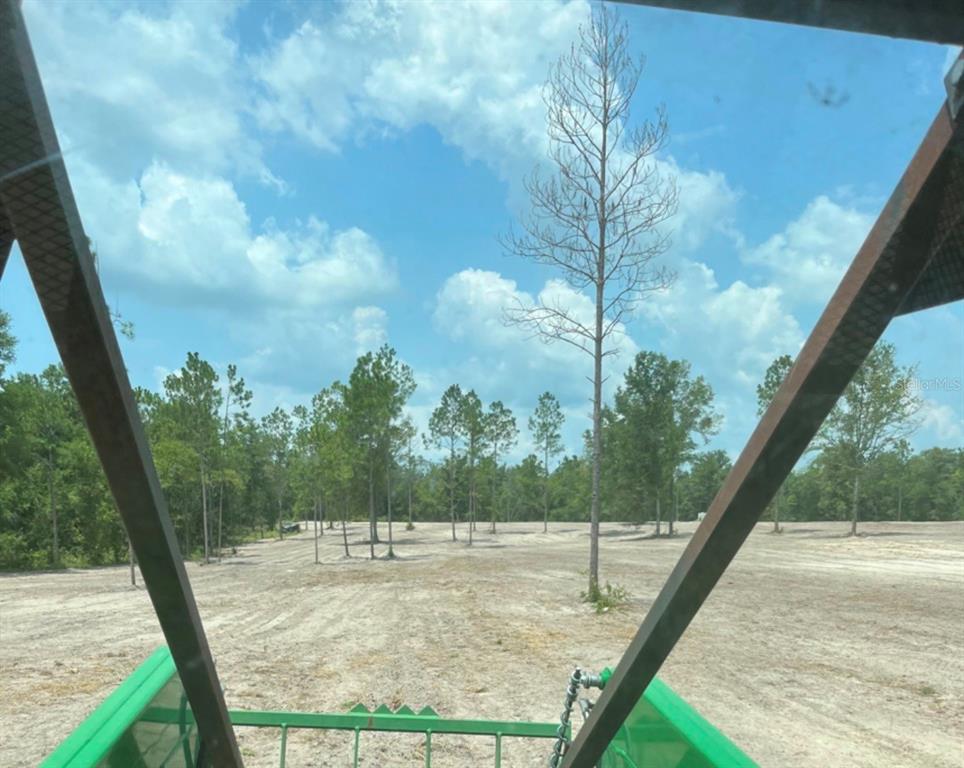 A view from inside a tractor cab looking out over a cleared, sandy lot with trees — 349C+R6, O'BRIEN, FL