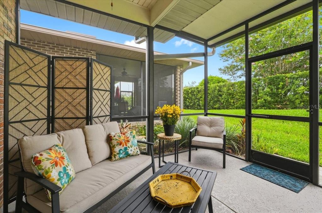 A brick house exterior features a screened-in porch, a grassy lawn, and a paved walkway — 730 MARTINIQUE CIRCLE, LAKELAND, FL
