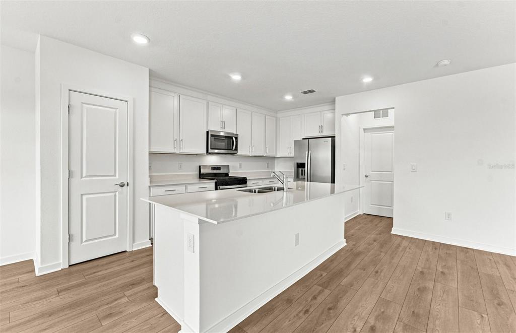An open-concept living room and kitchen featuring a grey sectional, round coffee table, and patio — 9877 TRELLIS VINE WAY, PARRISH, FL