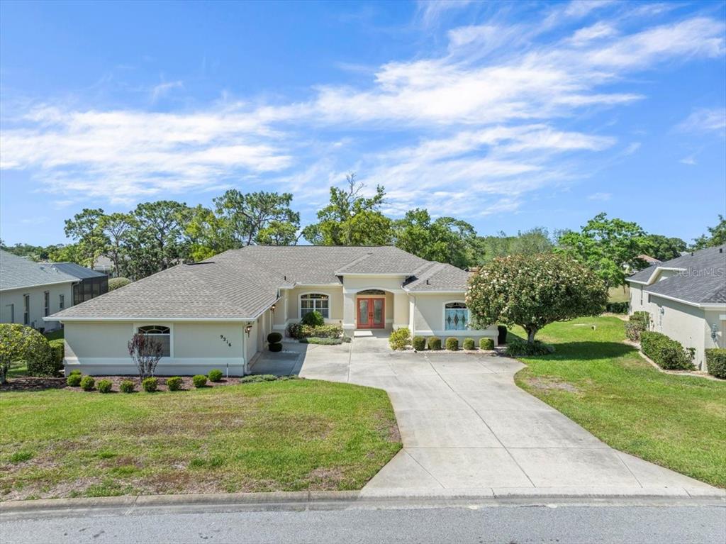 A single-story house with a beige exterior, a concrete driveway, and a large front lawn — 9216 TARLETON CIRCLE, WEEKI WACHEE, FL
