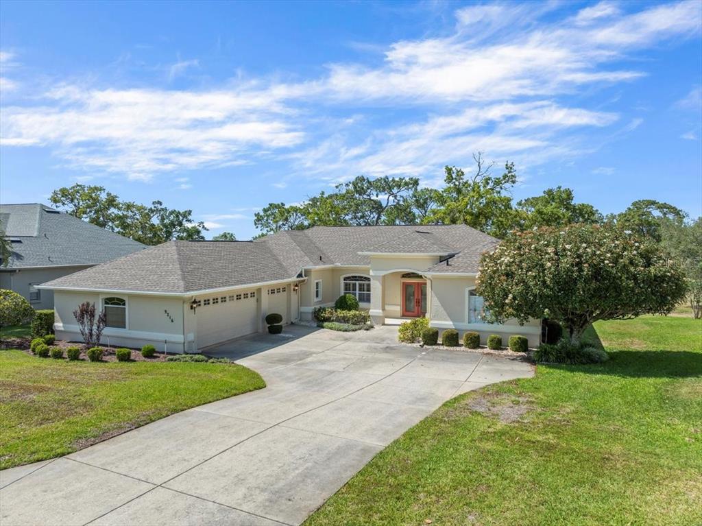 A single-story house with a beige stucco exterior, a gray shingled roof, and a driveway — 9216 TARLETON CIRCLE, WEEKI WACHEE, FL