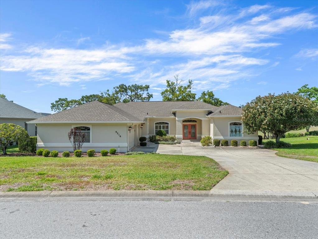 A single-story house with a beige stucco exterior, a gray roof, and a concrete driveway — 9216 TARLETON CIRCLE, WEEKI WACHEE, FL