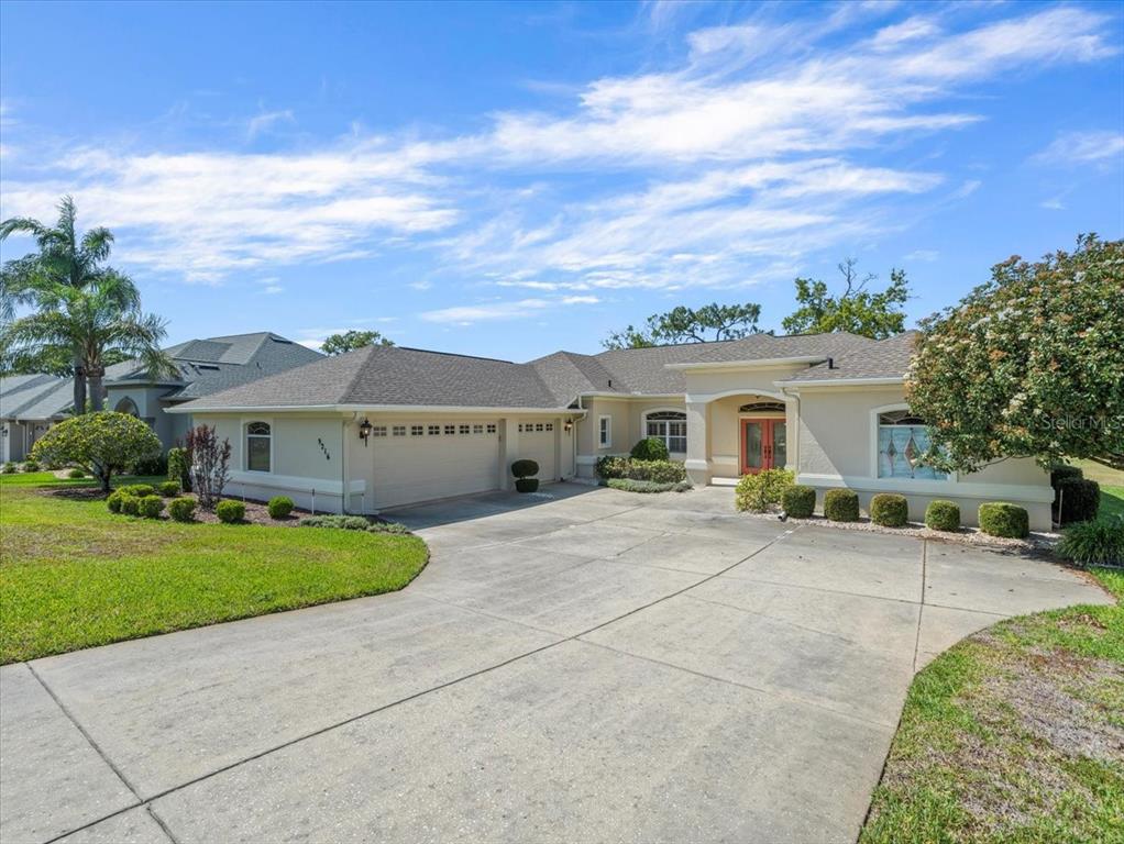 A single-story house with a beige exterior, a three-car garage, and a concrete driveway — 9216 TARLETON CIRCLE, WEEKI WACHEE, FL
