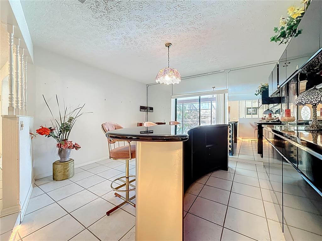 A kitchen features a curved black breakfast bar, pink stools, and white tile flooring — 452 SUMMIT CHASE DRIVE, VALRICO, FL