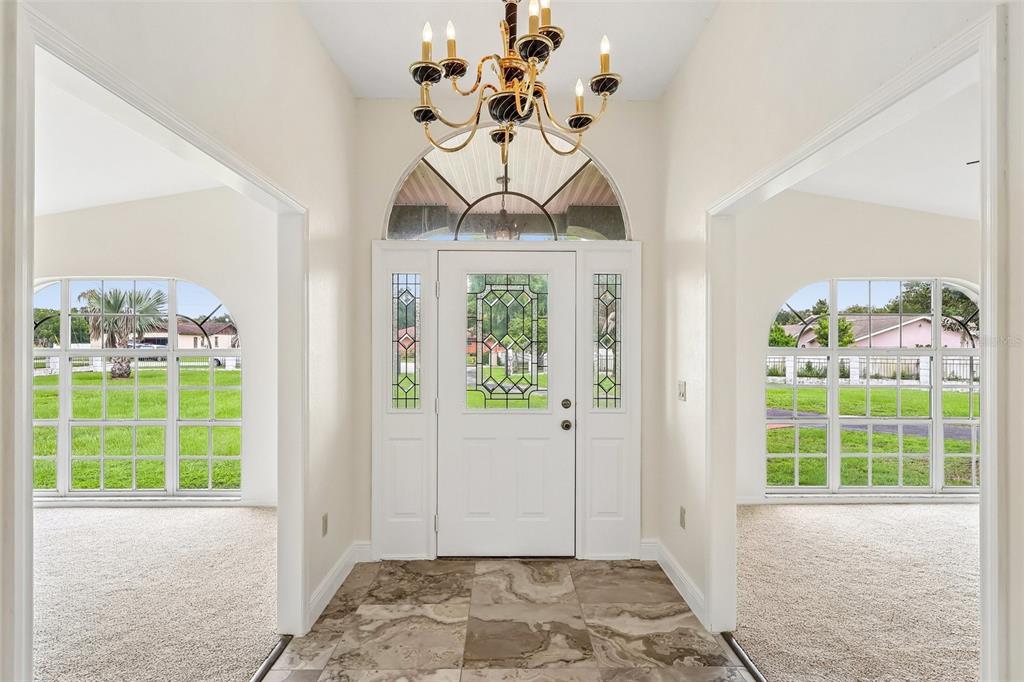 An entryway with tile flooring, a decorative front door, and a chandelier, virtually staged — 7026 PINEHAVEN DRIVE, LAKELAND, FL