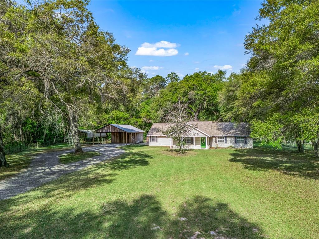 A covered concrete patio features two ceiling fans and overlooks a large, grassy backyard — 8234 S US 301, BUSHNELL, FL