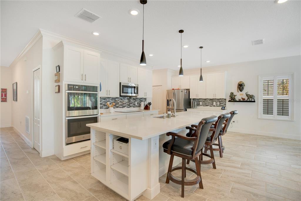 A modern kitchen features white cabinetry, a large quartz island, and stainless steel appliances — 260 JACKSON LOOP, DELAND, FL