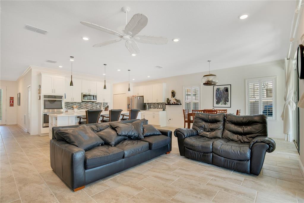 An open-concept living room and kitchen featuring white cabinetry, tile flooring, and leather furniture — 260 JACKSON LOOP, DELAND, FL