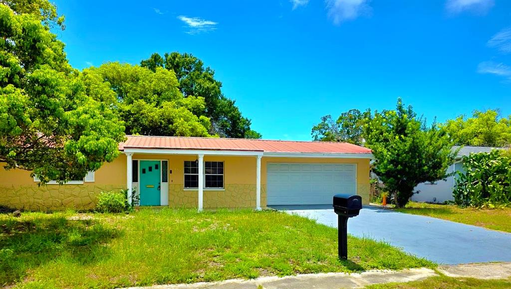 A single-story house with a yellow exterior, a metal roof, and a turquoise front door — 3150 FAIRMOUNT DRIVE, HOLIDAY, FL
