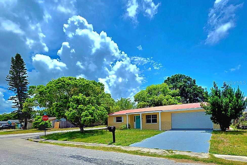 A single-story house with a yellow exterior, a red roof, and a concrete driveway — 3150 FAIRMOUNT DRIVE, HOLIDAY, FL