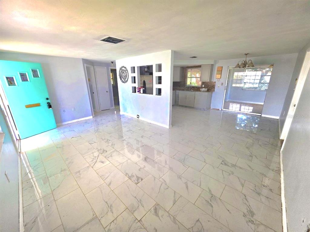 A living room with light-colored tile flooring, a bright blue front door, and an open kitchen — 3150 FAIRMOUNT DRIVE, HOLIDAY, FL