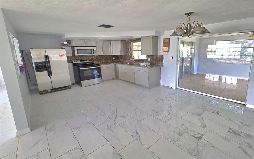 A kitchen features light gray cabinets, stainless steel appliances, and white marble-look tile flooring — 3150 FAIRMOUNT DRIVE, HOLIDAY, FL