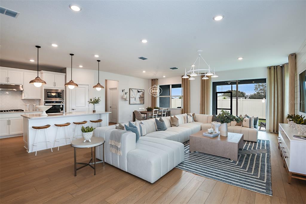 An open-concept living room and kitchen featuring a large sectional sofa and wood flooring — 9869 HICKORY PINES AVENUE, RIVERVIEW, FL