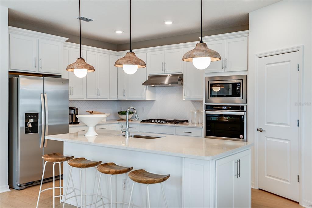 A modern kitchen features white cabinets, stainless steel appliances, a quartz island, and three barstools — 9869 HICKORY PINES AVENUE, RIVERVIEW, FL