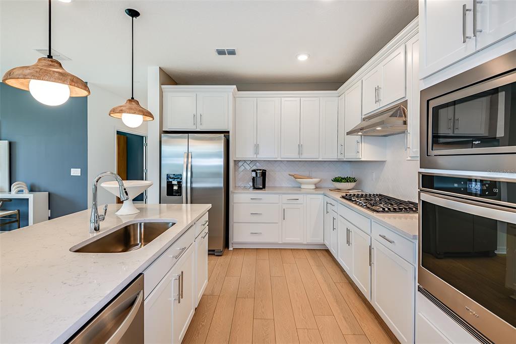 A modern kitchen features white cabinets, stainless steel appliances, a quartz island, and wood flooring — 9869 HICKORY PINES AVENUE, RIVERVIEW, FL