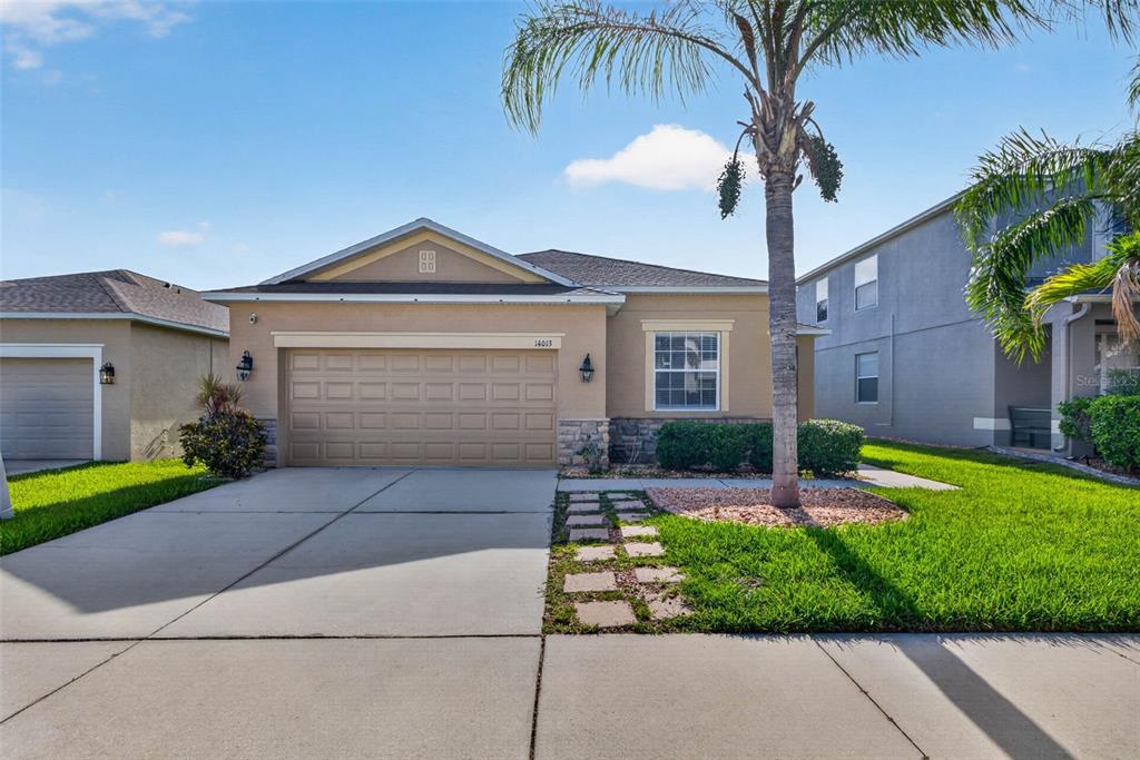 A single-story house with a tan stucco exterior, a two-car garage, and a palm tree — 14013 HOLLOW LEAF PLACE, RIVERVIEW, FL