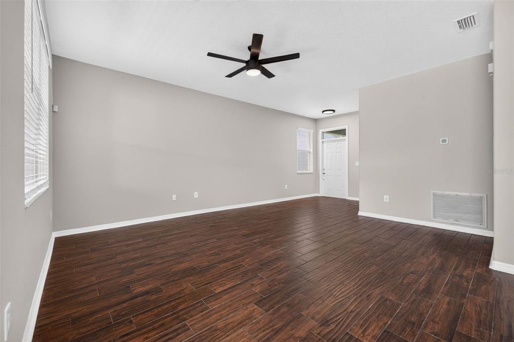 An empty living room features dark wood-look tile flooring, light gray walls, and a ceiling fan — 14013 HOLLOW LEAF PLACE, RIVERVIEW, FL