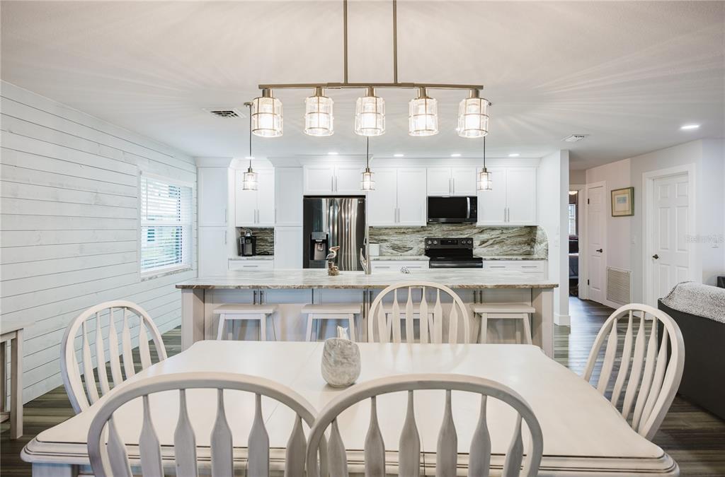 A living room with gray wood-look flooring, dark leather sofas, and an open kitchen beyond — 625 E BAFFIN DRIVE, VENICE, FL