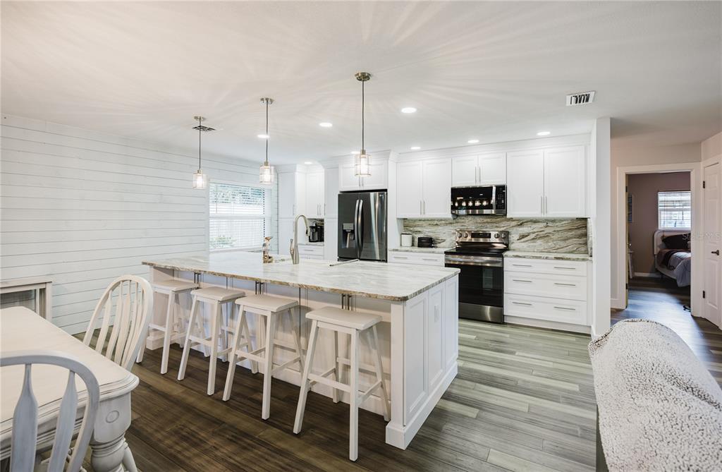 An open-concept living room and kitchen featuring wood-look tile flooring and white shiplap walls — 625 E BAFFIN DRIVE, VENICE, FL