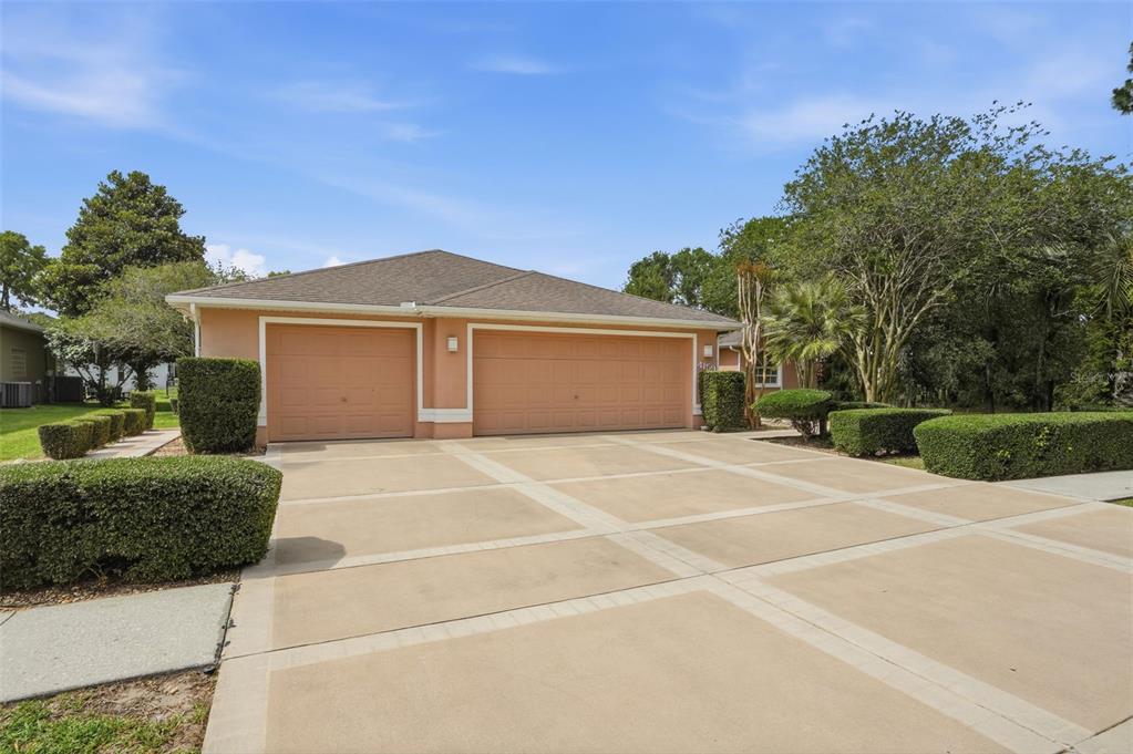 A single-story house with a three-car garage and a paved driveway surrounded by landscaping — 4159 ST IVES BOULEVARD, SPRING HILL, FL