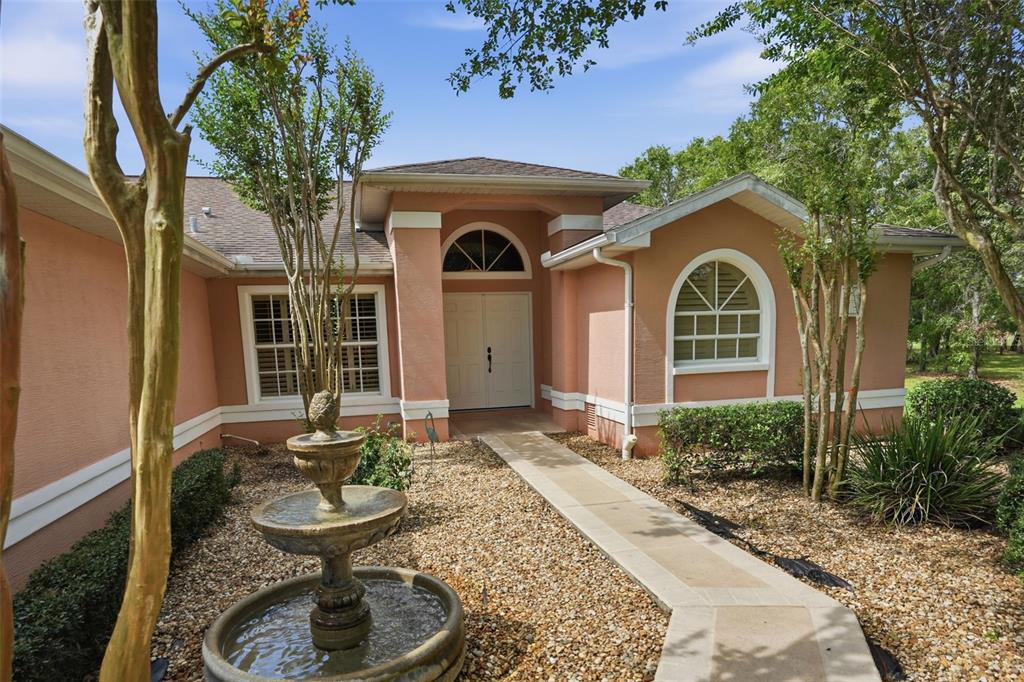 A peach-colored house with a stone fountain and a concrete walkway leading to the entrance — 4159 ST IVES BOULEVARD, SPRING HILL, FL