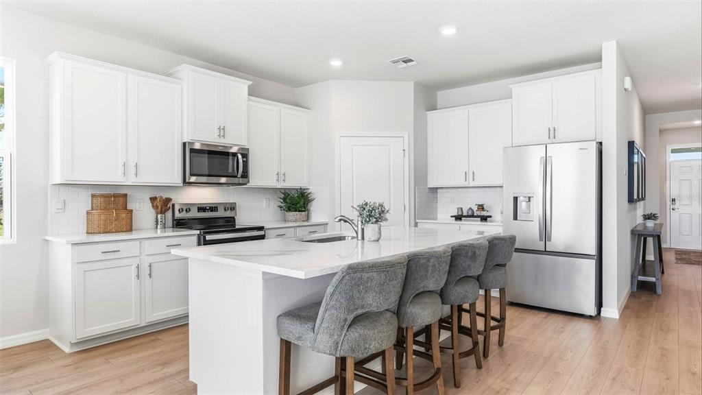 A modern kitchen with white cabinets, stainless steel appliances, a marble island, and gray stools — 17282 SALTBUSH TRAIL, PARRISH, FL
