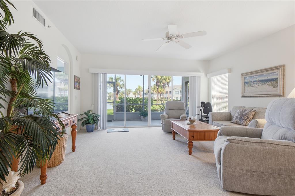A living room features light carpet, a ceiling fan, and sliding doors overlooking a patio — 418 LAUREL LAKE DRIVE UNIT 106, VENICE, FL