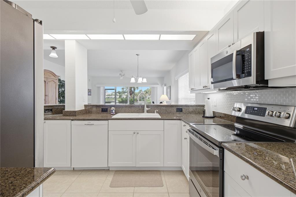 A white kitchen with stainless steel appliances and tile flooring leads to an arched hallway — 418 LAUREL LAKE DRIVE UNIT 106, VENICE, FL