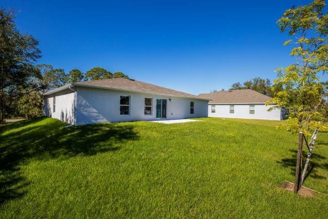 The rear exterior of a light-colored house features a sliding glass door and green lawn — 276 LUIS LANE, DEBARY, FL