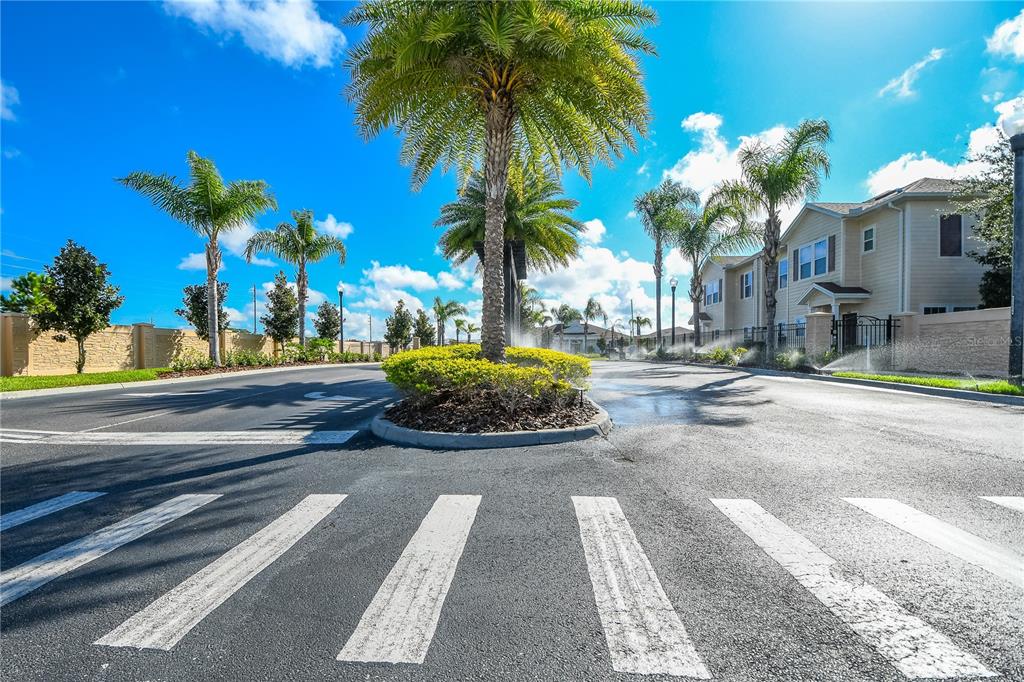 A paved road leads toward a landscaped median with palm trees and residential buildings — 8927 SHINE DRIVE, KISSIMMEE, FL