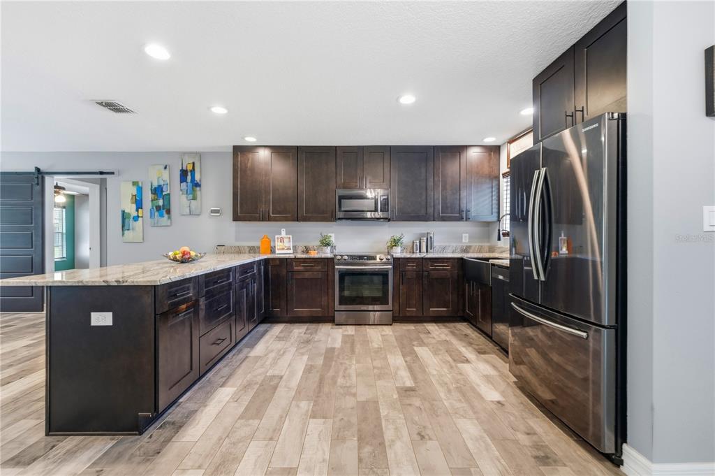 A kitchen with dark wood cabinets, stainless steel appliances, and a large granite-topped island — 10702 WILLIAM TELL DRIVE, ORLANDO, FL