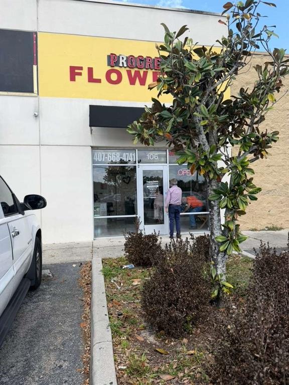 The exterior of a commercial building features a yellow sign and a glass entrance door — 7803 E COLONIAL DRIVE UNIT 106, ORLANDO, FL
