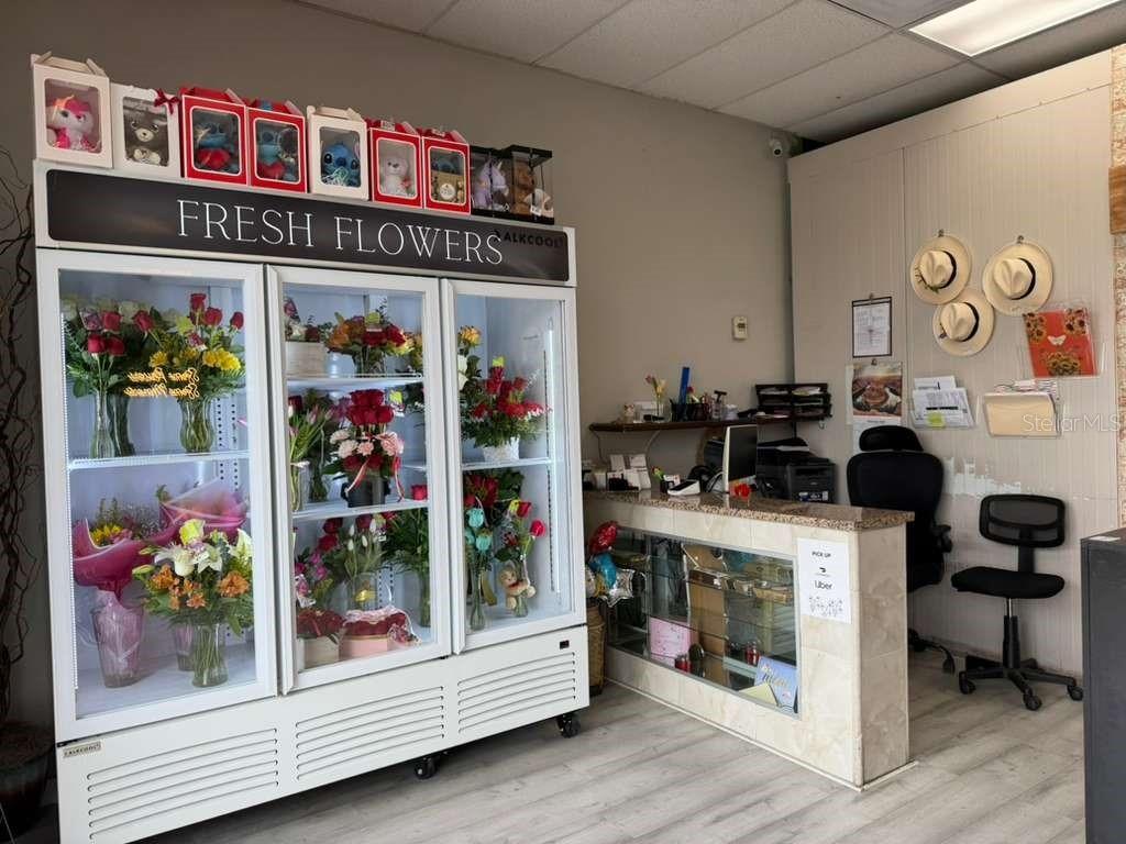 A floral shop interior features a large glass-front refrigerator, a service counter, and office chairs — 7803 E COLONIAL DRIVE UNIT 106, ORLANDO, FL
