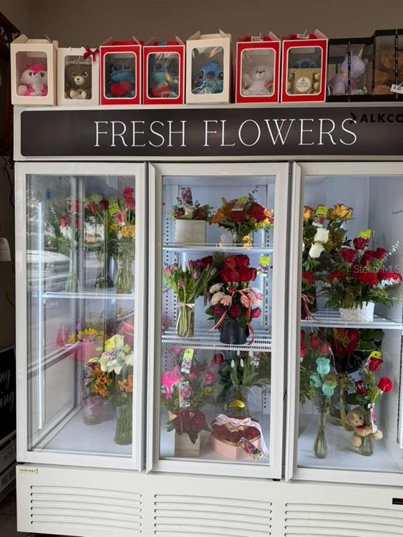 A commercial refrigerator filled with various floral arrangements sits beneath a row of gift boxes — 7803 E COLONIAL DRIVE UNIT 106, ORLANDO, FL