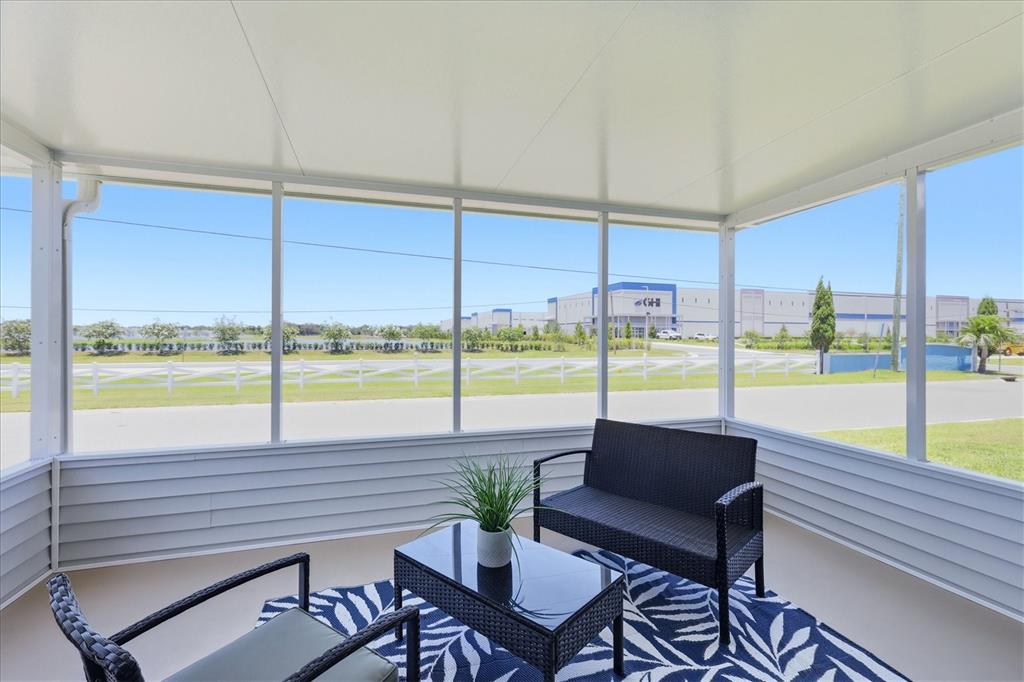 A screened-in porch features outdoor furniture on a patterned rug overlooking a large warehouse — 1536 45TH AVENUE E, ELLENTON, FL