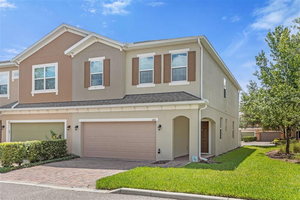 A two-story townhouse with a beige stucco exterior, a two-car garage, and brown shutters — 1160 PALMA VERDE PLACE, APOPKA, FL