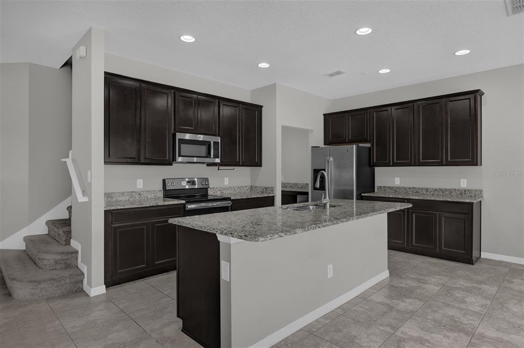 A kitchen features dark wood cabinets, granite countertops, a center island, and stainless steel appliances — 1160 PALMA VERDE PLACE, APOPKA, FL