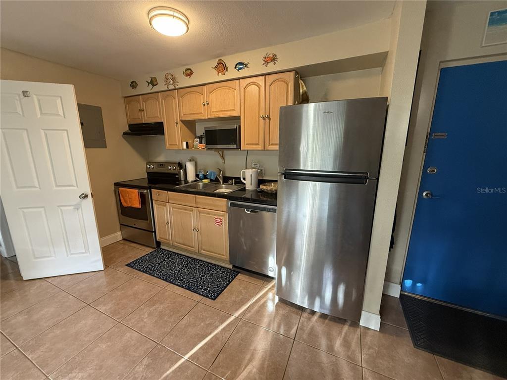 A kitchen features light wood cabinets, stainless steel appliances, and tan floor tiles — 4215 E BAY DRIVE UNIT 1702B, CLEARWATER, FL