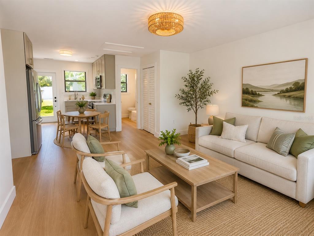 A bright living room and kitchen area features light wood flooring, neutral furniture, and greenery — 3219 E DEBAZAN AVENUE, ST PETE BEACH, FL