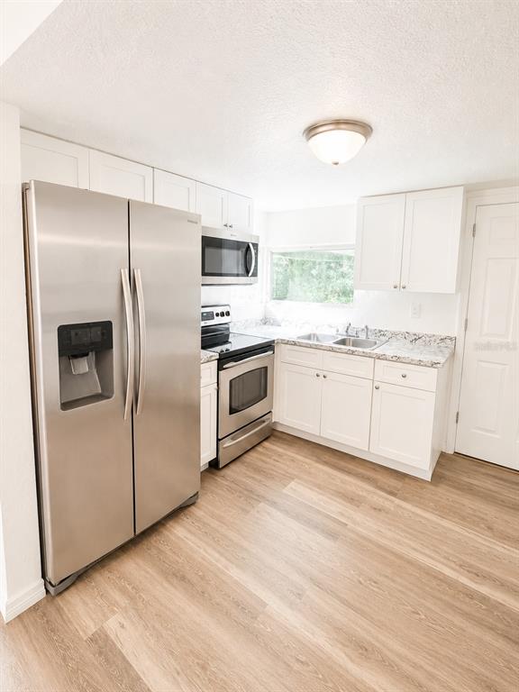 A kitchen features white cabinets, stainless steel appliances, granite countertops, and light wood-look flooring — 1052 OSCEOLA TRAIL, CASSELBERRY, FL