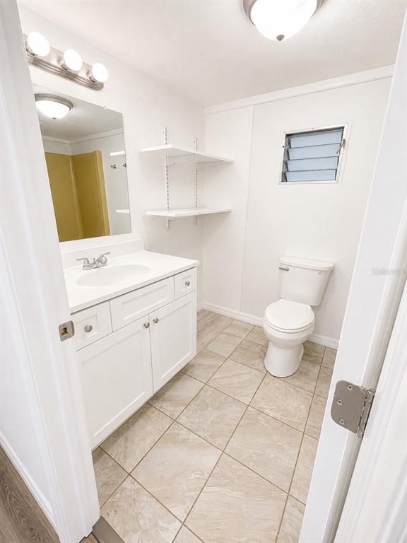 A bathroom features a white vanity, a toilet, wall-mounted shelves, and light-colored tile flooring — 1052 OSCEOLA TRAIL, CASSELBERRY, FL