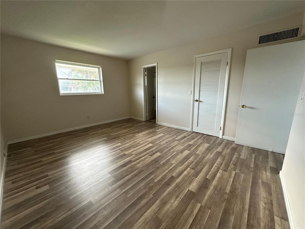 An empty bedroom features light-colored walls, wood-look flooring, a window, and two white doors — 809 HUMMINGBIRD WAY UNIT 5c, NORTH PALM BEACH, FL