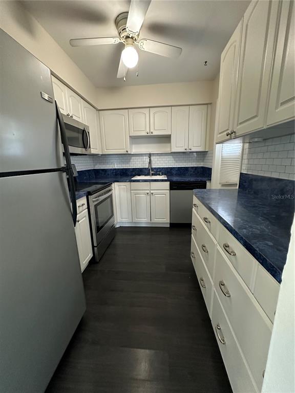 A kitchen features white cabinetry, dark blue countertops, stainless steel appliances, and dark wood flooring — 809 HUMMINGBIRD WAY UNIT 5c, NORTH PALM BEACH, FL