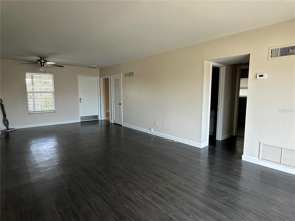An empty room features dark wood-look flooring, beige walls, a ceiling fan, and multiple doorways — 809 HUMMINGBIRD WAY UNIT 5c, NORTH PALM BEACH, FL